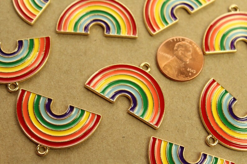 Peut inclure: Un groupe de breloques en m&eacute;tal en forme d'arc-en-ciel aux couleurs de l'arc-en-ciel. Les breloques ont une finition dor&eacute;e et sont &eacute;parpill&eacute;es sur une surface brune.