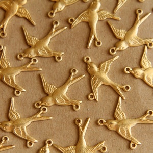 Könnte beinhalten: Eine Sammlung goldfarbener Vogel-Anhänger aus Metall mit schlichtem Design. Die Anhänger haben alle die Form eines Vogels mit ausgebreiteten Flügeln.