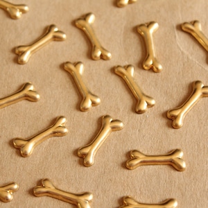 May include: A collection of gold-colored bone-shaped charms scattered on a brown surface.