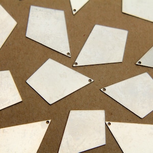 May include: A collection of silver-colored metal diamond-shaped charms with a hole at the top. The charms are scattered on a brown surface.
