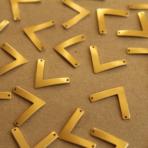 May include: A collection of gold-coloured metal corner brackets, scattered on a brown surface. The brackets are all the same size and shape, with a right angle and two holes on each side.