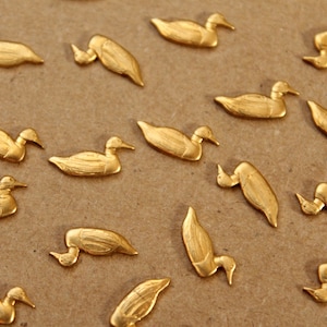 May include: A collection of gold-colored metal duck figurines. The ducks are arranged in a scattered pattern on a brown surface.