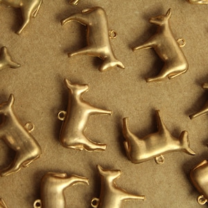 May include: A collection of gold-colored metal cow charms, each with a unique pose. The charms are scattered on a brown surface.
