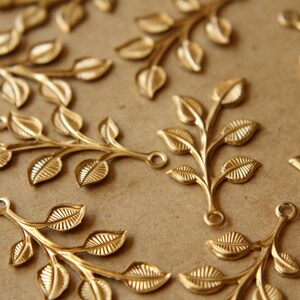 May include: A collection of gold-toned metal leaf branch charms with a loop at the top for attaching to jewelry or other crafts.