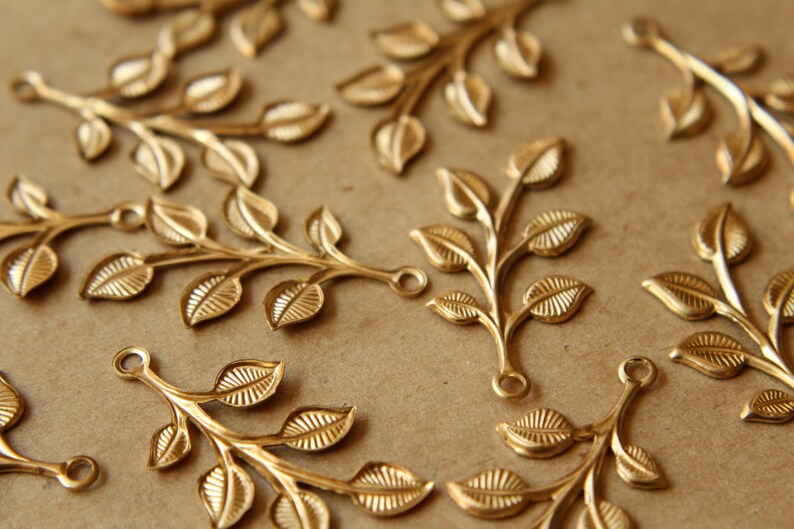 May include: A collection of gold-toned metal leaf branch charms with a loop at the top for attaching to jewelry or other crafts.