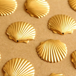 Puede incluir: Una colección de diez conchas doradas dispuestas sobre una superficie marrón. Las conchas son todas del mismo tamaño y forma, y tienen un acabado liso y brillante.