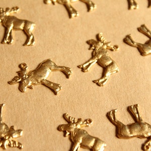 May include: A collection of gold-colored moose charms, each with a unique design. The charms are arranged on a brown surface.