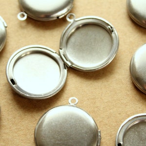 May include: A group of eight silver locket pendants with a hinged opening. The lockets are round and have a smooth, polished finish.