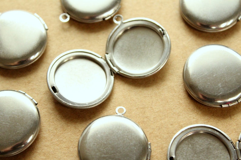 May include: A group of eight silver locket pendants with a hinged opening. The lockets are round and have a smooth, polished finish.