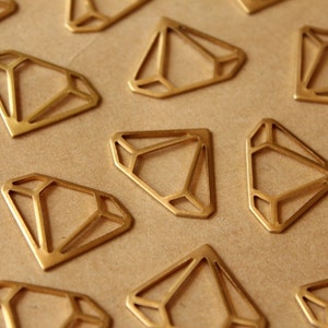May include: A collection of gold-coloured metal diamond shapes, each with a geometric design, arranged on a brown surface.