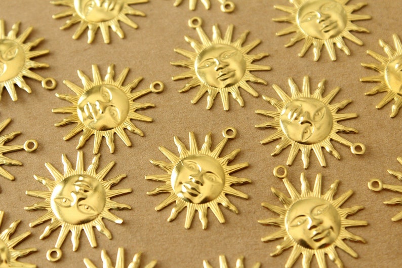 May include: A collection of gold-toned metal sun charms with a face design. Each charm has a loop for attaching to a necklace, bracelet, or other jewelry.