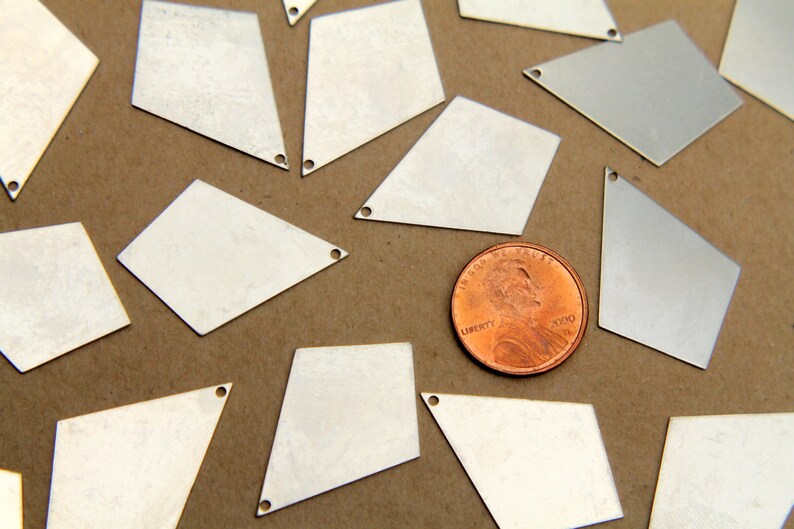 May include: A collection of silver-colored metal diamond-shaped charms with a hole at the top. The charms are scattered on a brown surface with a penny in the center.