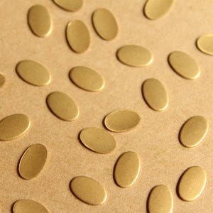 May include: A collection of small, oval-shaped, gold-colored metal pieces scattered on a brown surface.