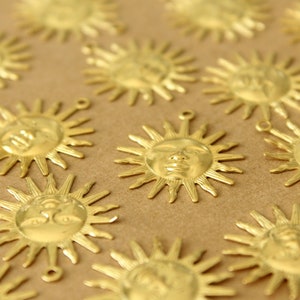 May include: A collection of gold-toned metal sun charms with a face design. The charms are scattered on a brown surface.