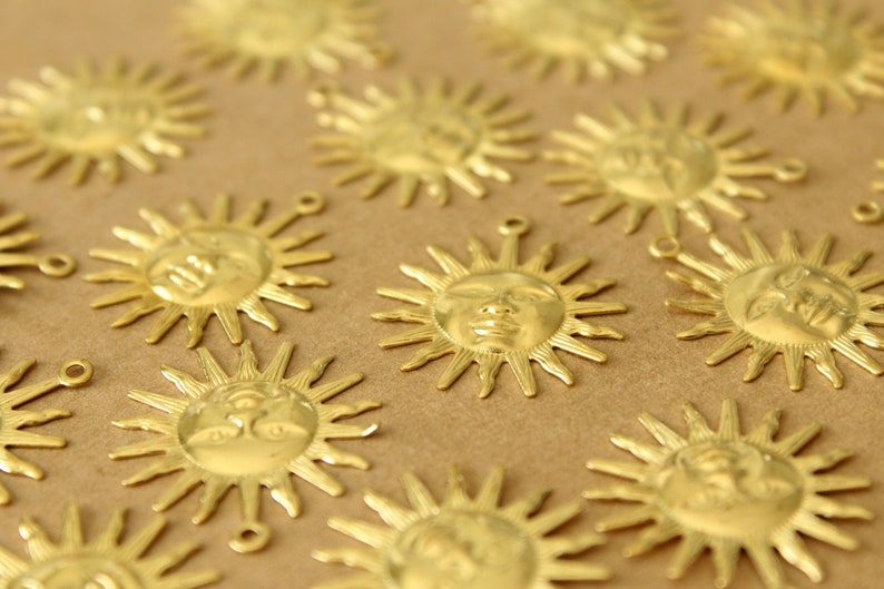May include: A collection of gold-toned metal sun charms with a face design. The charms are scattered on a brown surface.