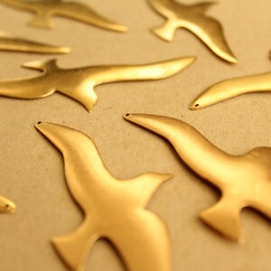 May include: A set of seven gold-colored metal bird cutouts. The birds are all facing the same direction and are arranged in a random pattern.