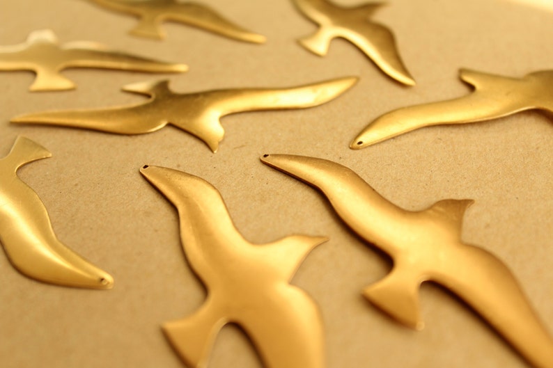 May include: A set of seven gold-colored metal bird cutouts. The birds are all facing the same direction and are arranged in a random pattern.