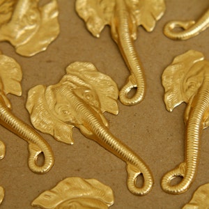 Op de afbeelding: Een verzameling gouden metalen olifantenbedels met gedetailleerde kenmerken. De bedels hebben een getextureerd oppervlak en een lus aan de onderkant om aan sieraden of andere knutselwerken te bevestigen.