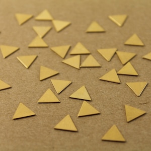 May include: A collection of small, gold-colored triangle shapes scattered on a brown surface.