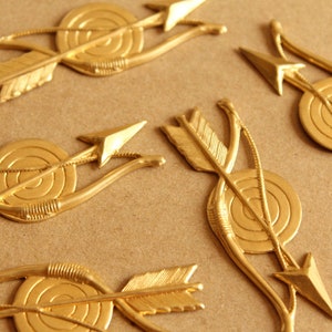 May include: Five gold-coloured arrow and target decorations. Each decoration features a stylised arrow and target with a concentric circle design.