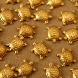 Peut inclure: Une collection de figurines de tortues dorées, chacune avec un design de carapace détaillé. Les tortues sont disposées sur une surface brune.