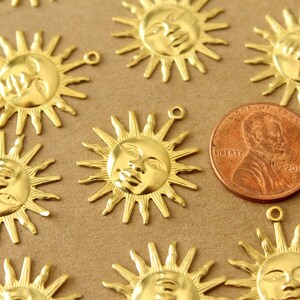 May include: A close-up of a group of gold-colored metal sun charms with a face design. The charms are about the size of a US penny.