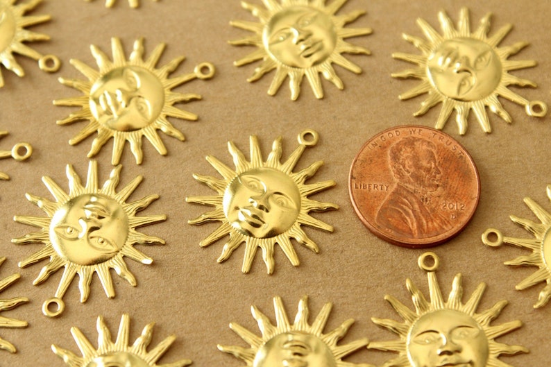 May include: A close-up of a group of gold-colored metal sun charms with a face design. The charms are about the size of a US penny.