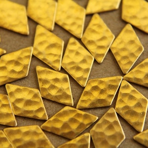 Puede incluir: Primer plano de un grupo de piezas metálicas de forma de diamante de color dorado. Las piezas tienen una textura martillada y están dispuestas en un patrón aleatorio.