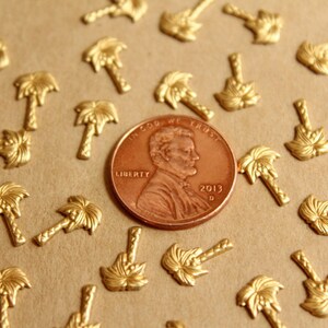 May include: A close-up of a US penny coin with the year 2013 on it, surrounded by many small gold palm tree charms. The coin is in focus, and the charms are out of focus.