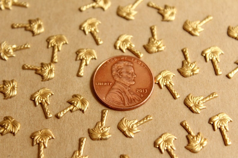 May include: A close-up of a US penny coin with the year 2013 on it, surrounded by many small gold palm tree charms. The coin is in focus, and the charms are out of focus.