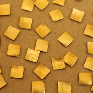 May include: A collection of small, square, gold-colored metal tiles scattered on a brown surface.
