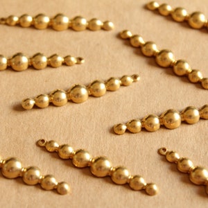 May include: A collection of gold-toned metal bead chains, each featuring a row of round beads. The chains are arranged in a staggered pattern on a brown surface.