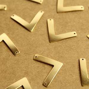 May include: A group of gold-coloured metal corner brackets with two holes in each. The brackets are arranged in a pattern on a brown surface.