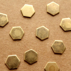 May include: A close-up of a group of 14 gold-colored hexagonal metal pieces on a brown surface.