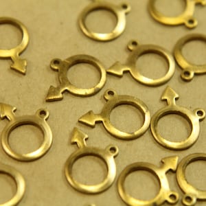 May include: A group of gold-colored metal charms in the shape of a circle with an arrow pointing to the right. The charms are scattered on a brown surface.