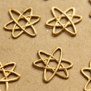 May include: A collection of gold-colored metal charms shaped like stylized atoms. The charms are arranged on a brown surface.