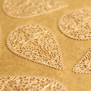 Op de afbeelding: Een set van zes goudkleurige metalen versieringen in de vorm van een traan met een delicaat bloemenpatroon.