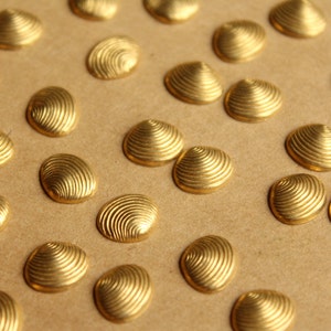 May include: A close-up of a group of gold-coloured metal decorative accents shaped like seashells. The accents have a textured, ribbed surface and are arranged on a brown background.