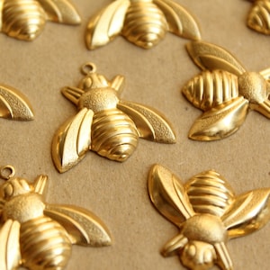 Könnte beinhalten: Eine Sammlung von goldfarbenen Bienenanhängern mit filigranen Details. Die Bienen sind in einem zufälligen Muster auf einer braunen Oberfläche angeordnet.
