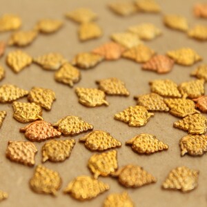 May include: A collection of gold-colored metal charms shaped like grape clusters. The charms are scattered on a brown surface.