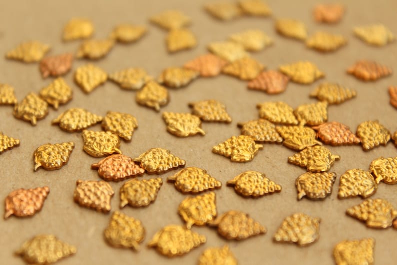May include: A collection of gold-colored metal charms shaped like grape clusters. The charms are scattered on a brown surface.