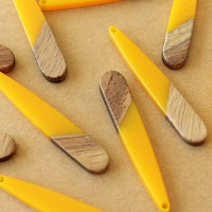 May include: A collection of yellow and brown wooden and resin pendant earrings. Each earring is a long, thin oval shape with a yellow resin top and a brown wood bottom.