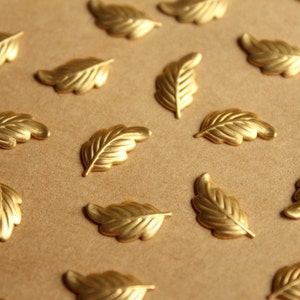 May include: A collection of gold-colored metal leaf-shaped embellishments on a brown background.