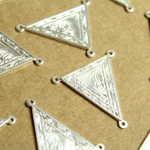 Peut inclure: Gros plan sur plusieurs pendentifs en argent de forme triangulaire avec des motifs floraux complexes. Chaque pendentif a trois petites boucles pour l'attacher à une chaîne ou à d'autres bijoux.