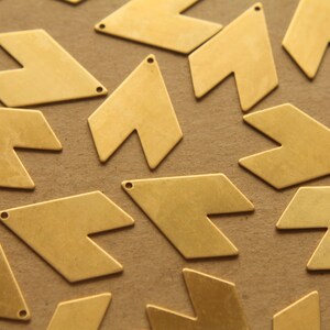 May include: A group of gold-colored metal arrow shapes, scattered on a brown surface. The arrow shapes have a pointed tip and a slightly curved base.