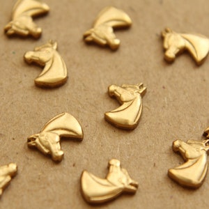 May include: A collection of small, gold-colored horse head charms. The charms are scattered across a neutral-toned surface. The horse heads are detailed with a mane and facial features, suitable for jewelry making or crafts.