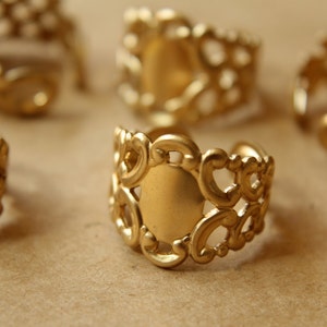 May include: Six gold-toned metal rings with intricate filigree designs. The rings have a circular opening in the center, suggesting they are meant to be used as decorative embellishments or for crafting.