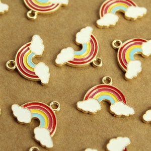 Könnte beinhalten: Eine Gruppe goldfarbener Regenbogen-Anhänger mit weißen Wolken. Jeder Anhänger hat einen roten, gelben, blauen und hellblauen Regenbogen mit einer goldenen Öse zum Anbringen an eine Halskette oder ein Armband.