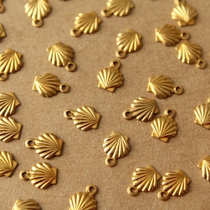 May include: A collection of gold-colored metal seashell charms with a loop at the top. The charms are scattered on a brown surface.