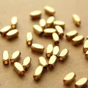 May include: A scattering of gold-colored metal beads, each with a slightly oval shape. The beads are scattered on a brown surface.